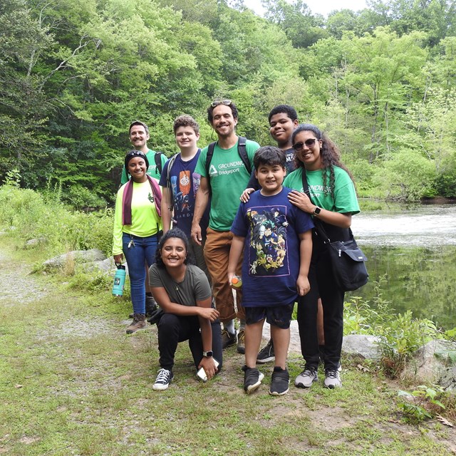 A group of people standing in front of a pond on a sunny day.