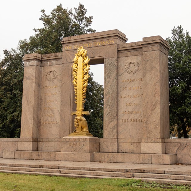 A stone monument with a statue of a hand holding a flaming golden sword in the center.