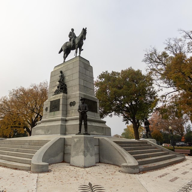 A statue of General William Tecumseh Sherman riding a horse on top of a large stone pedestal.