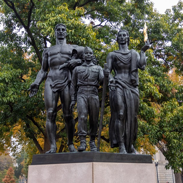 A bronze statue of a boy flanked by a man and woman.