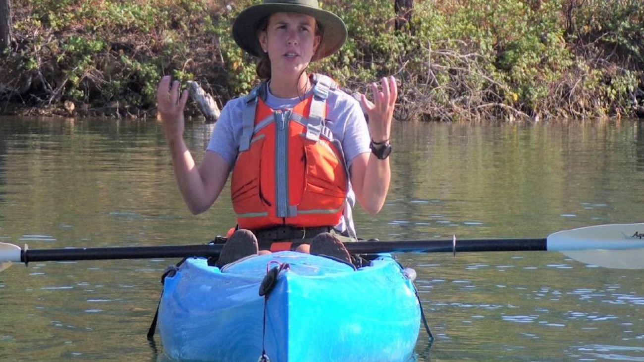 Female park ranger in kayak with hands raised.