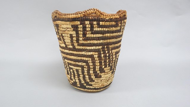 A woven basket with a grey background. The basket has a geometric line patterns across it.