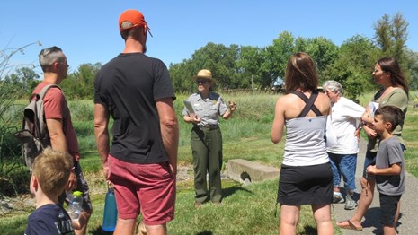 A ranger stands in front of a group of 8 visitors in a grass area