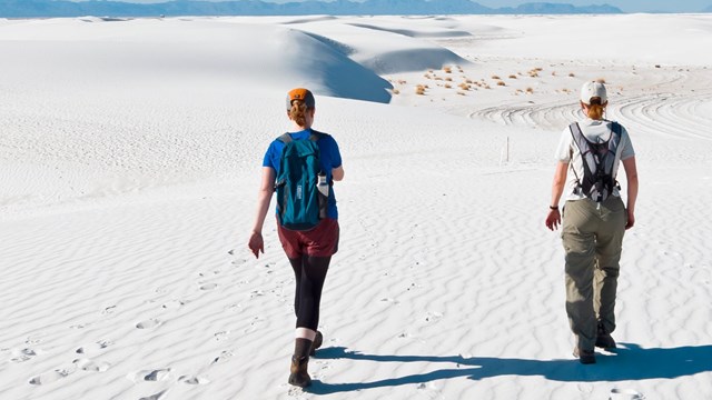 two people hiking on white sand dunes.
