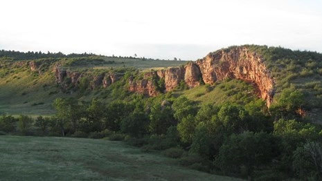 A cliff of red rocks protrudes from the surrounding hills.