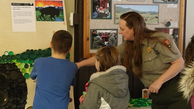 A ranger with three children creating a mosaic with plastic bottle caps