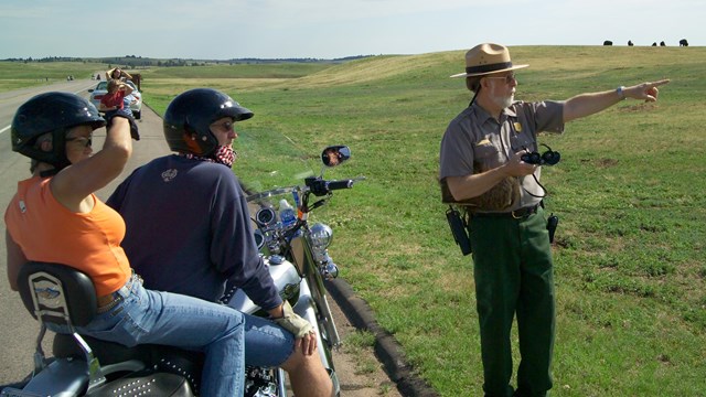 A ranger points in the distance as visitors look into the open prairie