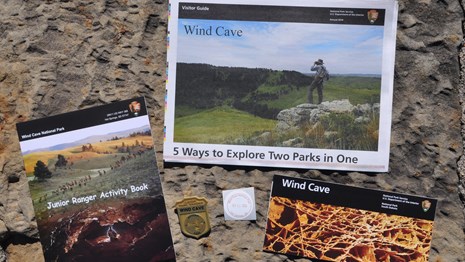 a park newspaper, brochure, junior ranger book, badge, and park stamp against stone