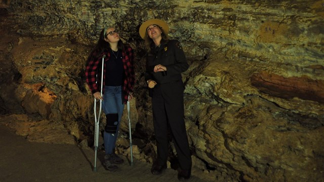 a park ranger next to a visitor on crutches in a dim cave room 