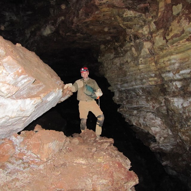 a man in caving gear standing on a rock in a dim, large cave room