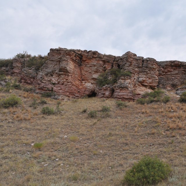 a short reddish stone cliff above a grassy meadow