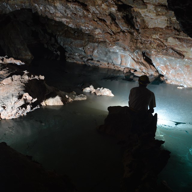 a caver sitting on the edge of a clear blue underground lake