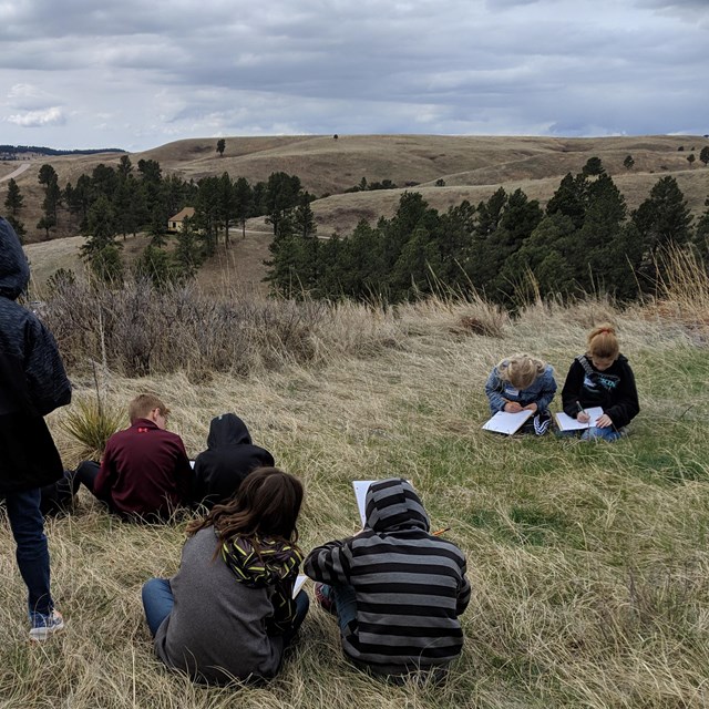 Children on a hillside drawing what they see.