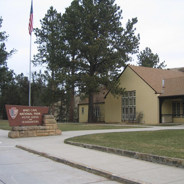 a large yellow building with brown trim and a brown roof with a park sign and flag in front of it