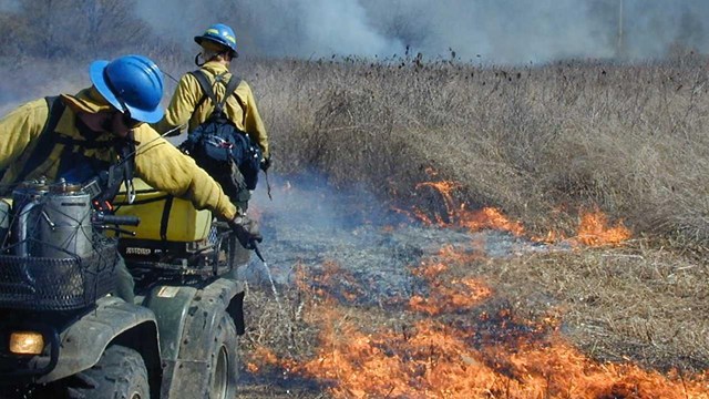 Firefighters dose fire on a field with water as they drive by in a ATV. 