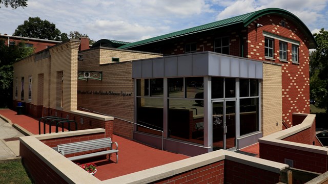 A red and yellow brick building with large glass windows and doors in the front corner