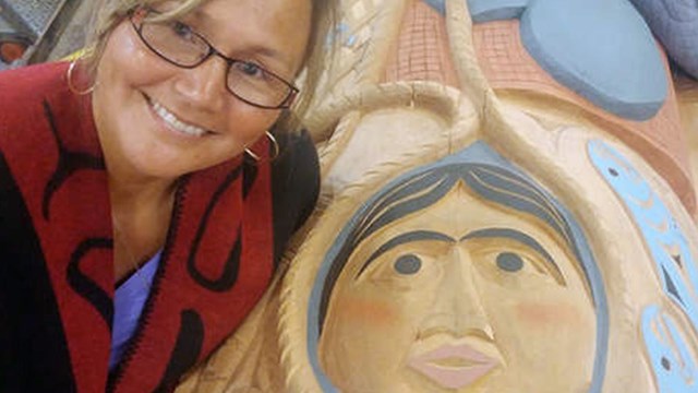 Woman smiles at camera, standing over bright carvings of face