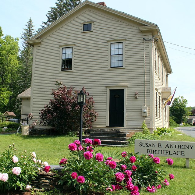 Photo of the exterior of the Susan B Anthony birthplace with flowers blooming
