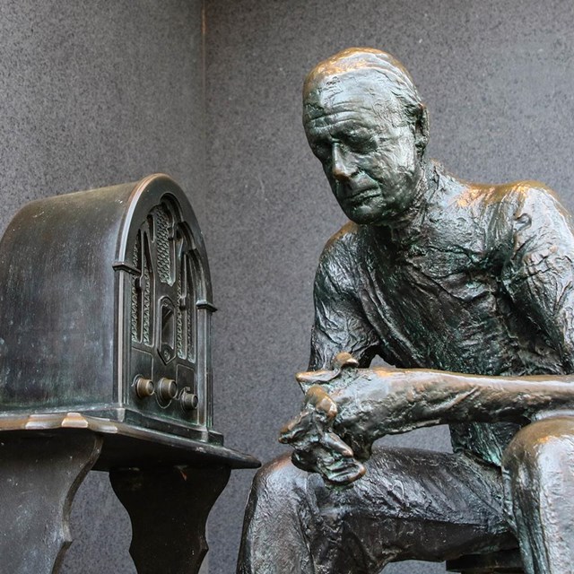 Color photo of a statue, person listening to an old fashioned radio