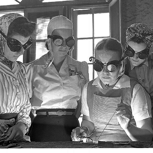 Group of women crowded around science experiment wearing goggles. 
