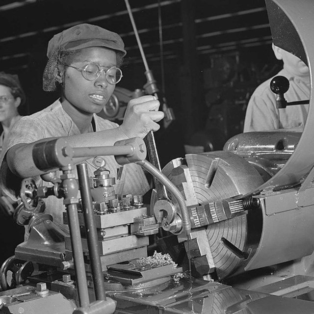 African American woman works machinery in factory.