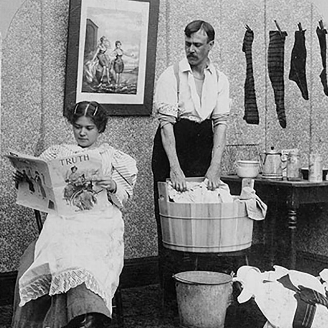 Woman reading newspaper while man washes the laundry