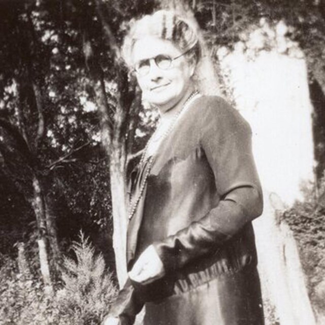 A woman stands in a garden. Black and white photo. Wikimedia