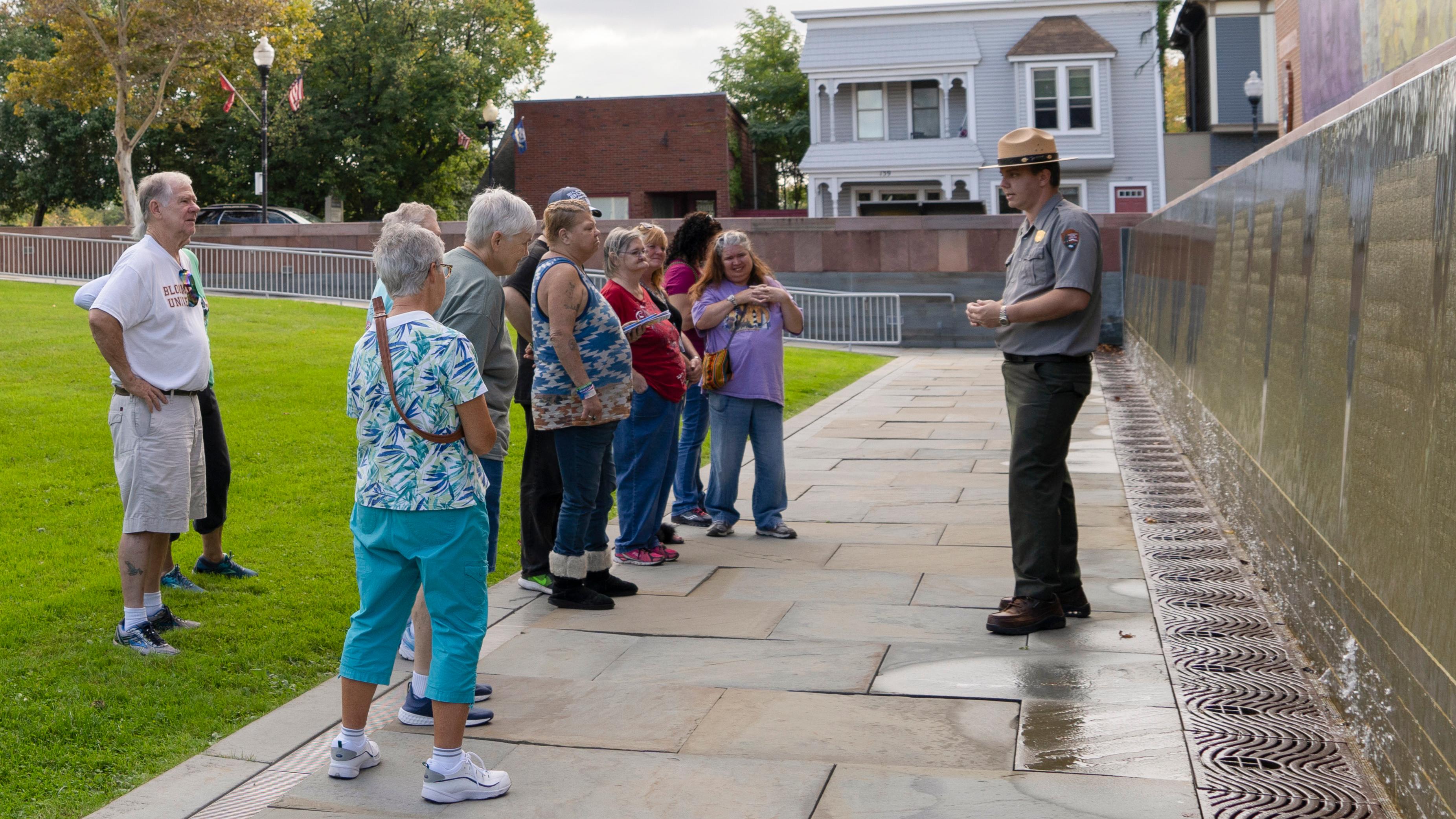 A ranger stands in front of the Waterwall and speaks to a group of visitors.