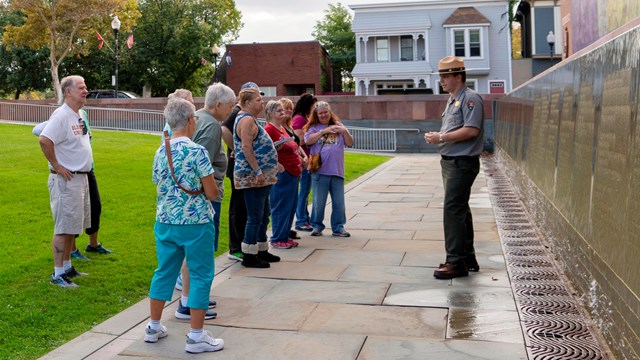 A ranger stands in front of the Waterwall and speaks to a group of visitors.
