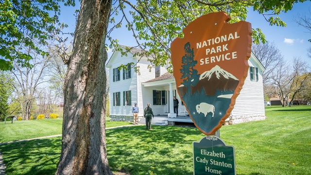 A large carved National Park Service arrowhead standing in front of a white house.
