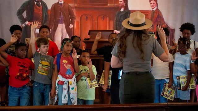 A park ranger speaks to a group of children facing the camera. 