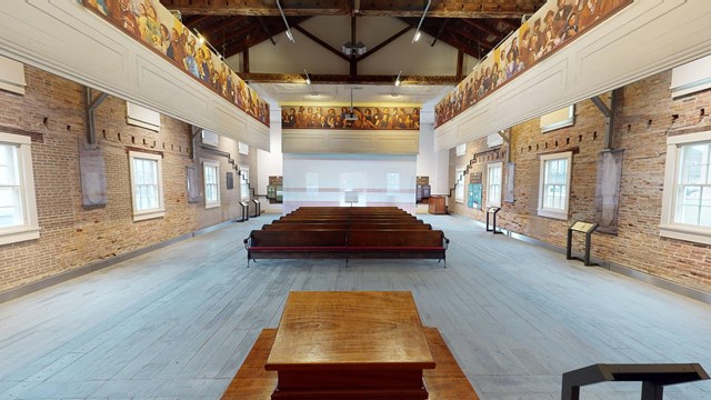 A wide-angle view of the Wesleyan Chapel interior, looking from the podium out toward rows of pews.