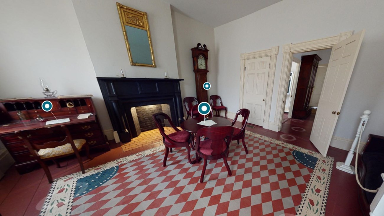 A wide-angle image showing a sparsely-decorated room, with a patterned floor canvas and a tea table.
