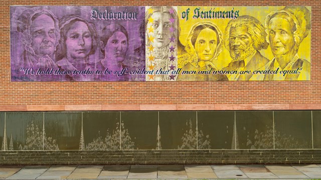 West side of the visitor center with a large mural of portraits in purple, black and gold.