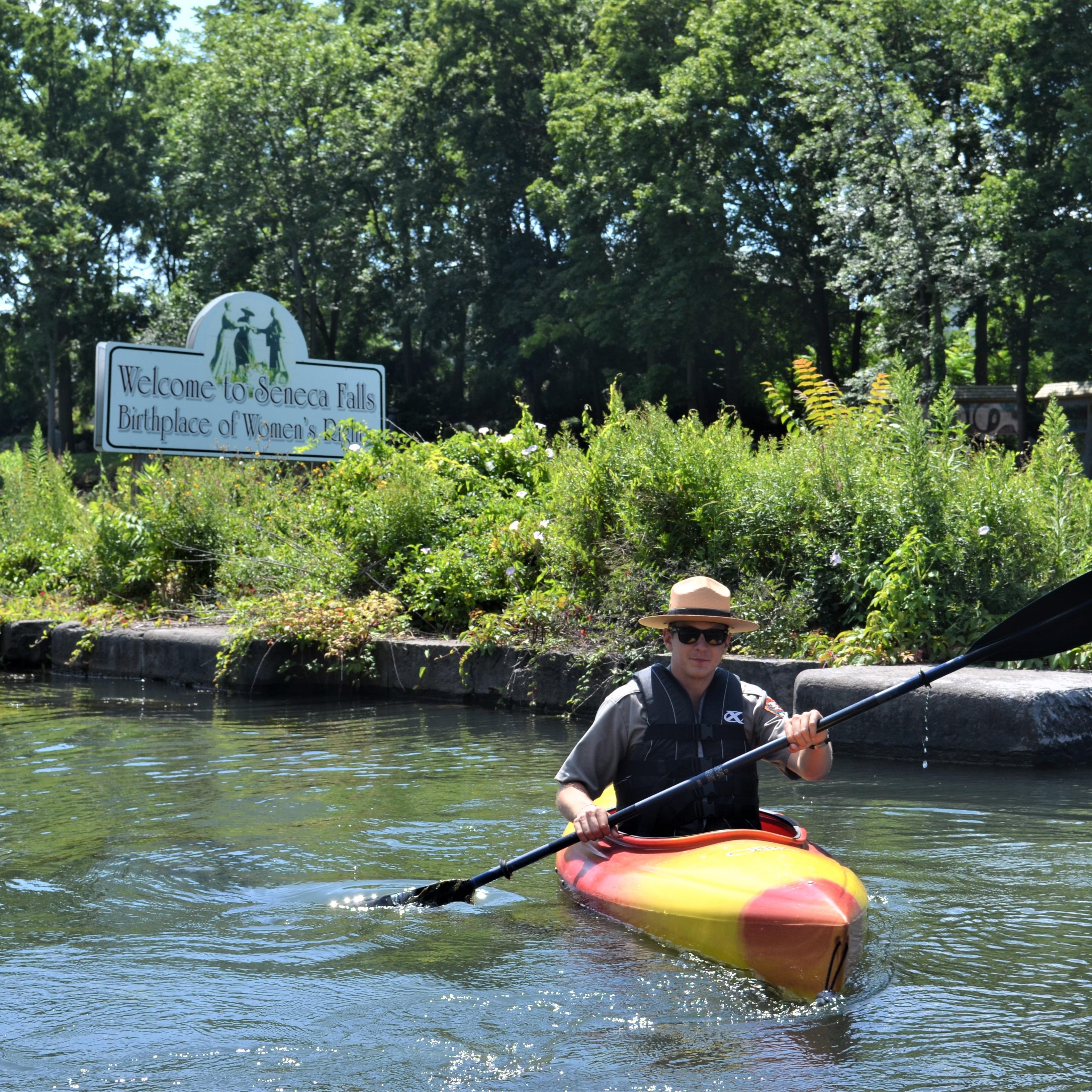 A ranger paddling a kayak past a sign for Seneca Falls