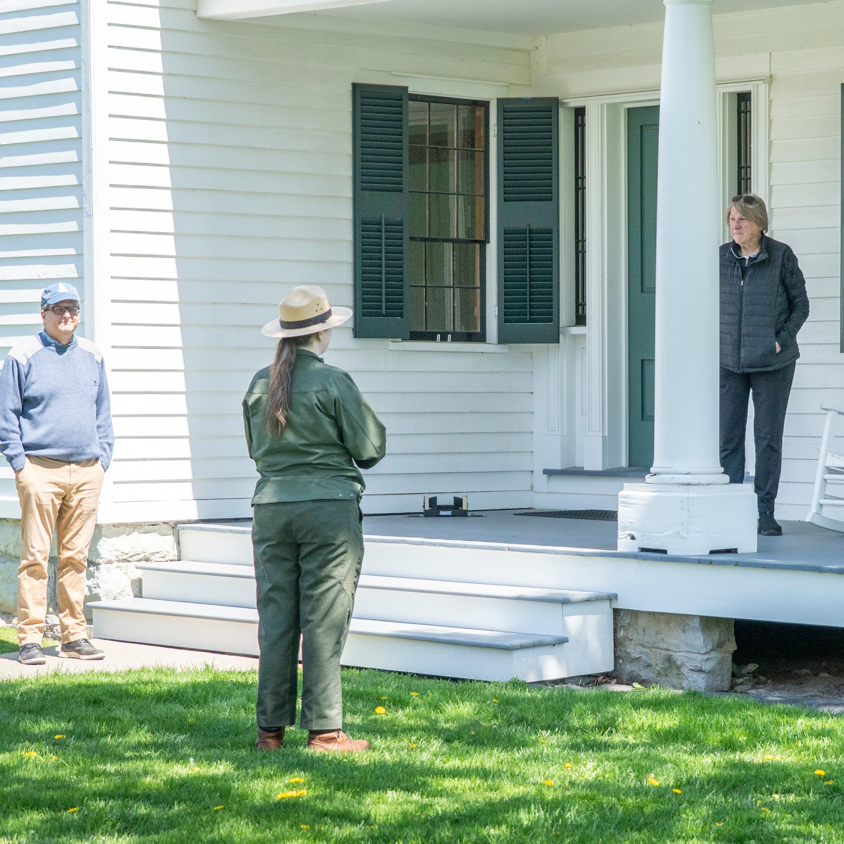 A ranger standing in front of a porch speaking to people.