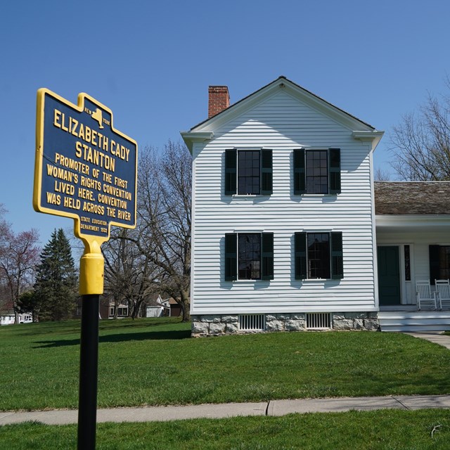 A two-story white house with a blue and yellow historic marker in front.
