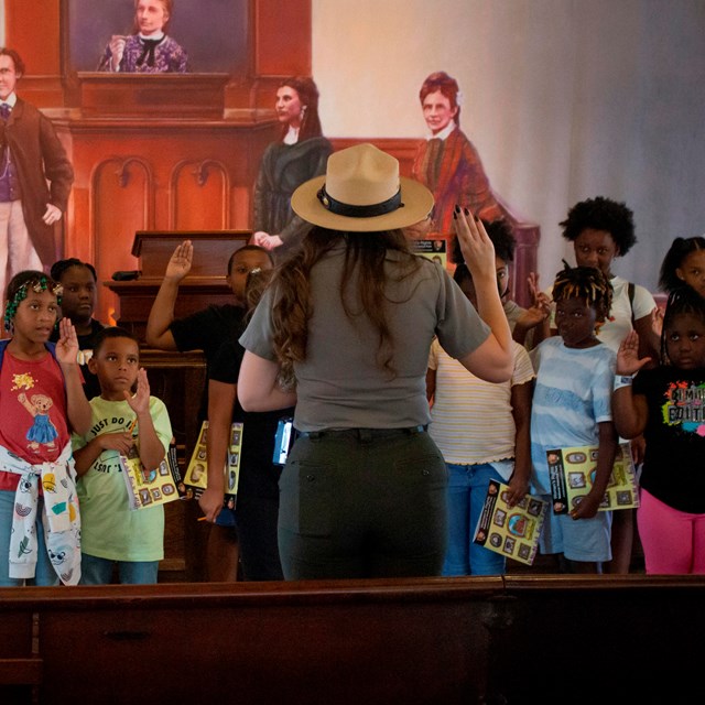 A park ranger speaks to a group of children facing the camera. 