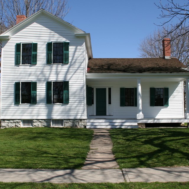 A two-story white house with a porch and green shutters.