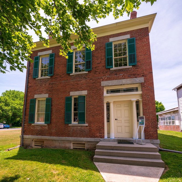 A two-story red brick house with green shutters.