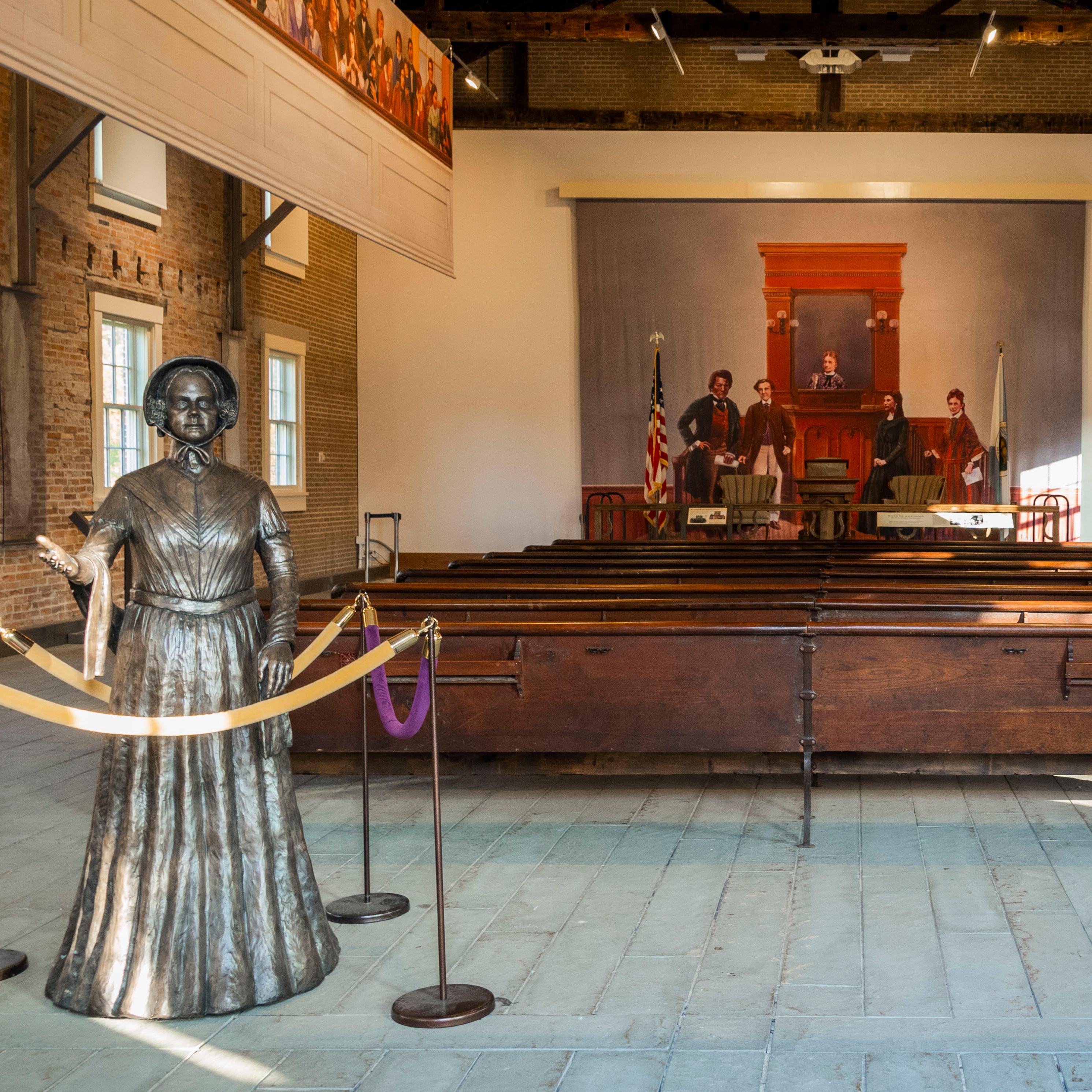 An empty room full of benches, with a statue of a woman welcoming in the foreground.