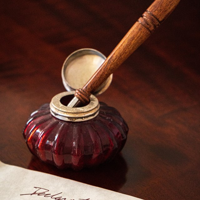 A pen sitting in an inkwell next to a piece of paper.