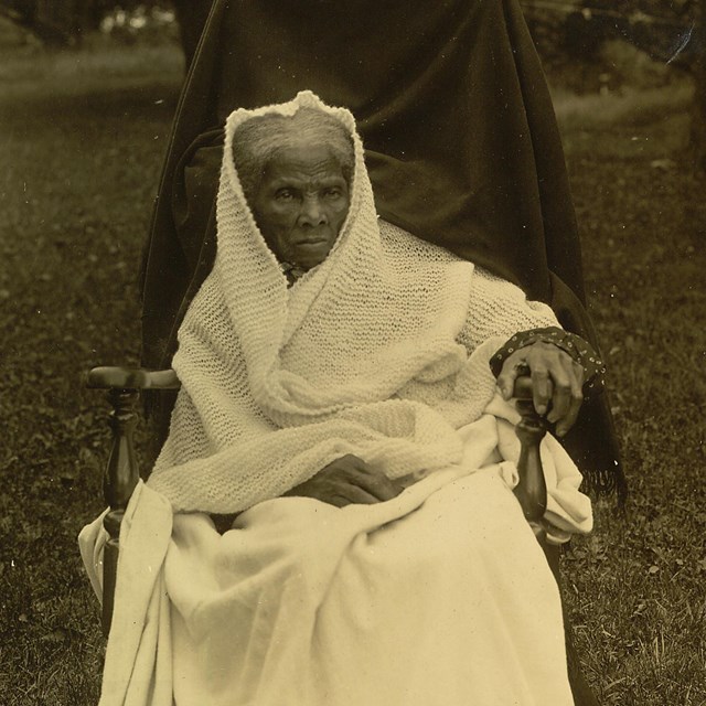 An elderly woman sitting in a chair outdoors.