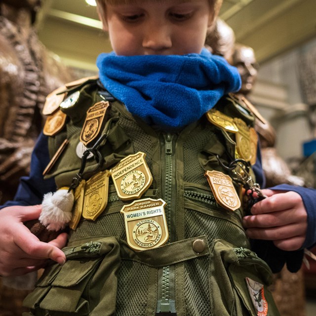 A child shows off his vest adorned with various Junior Ranger badges.