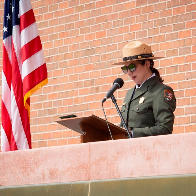 Superintendent Ahna Wilson speaks at a lectern in front of the visitor center wall.