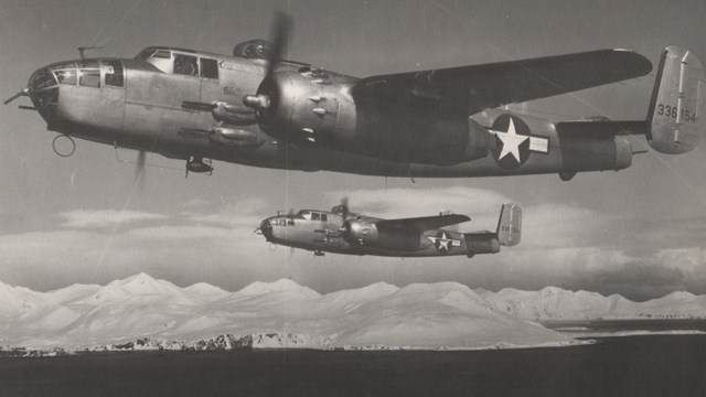 Black and white photo of two airplanes with clouds in background.