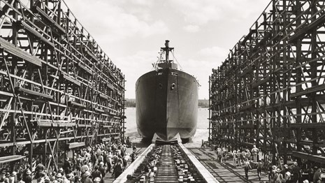 Ship launching from dry dock as workers look on