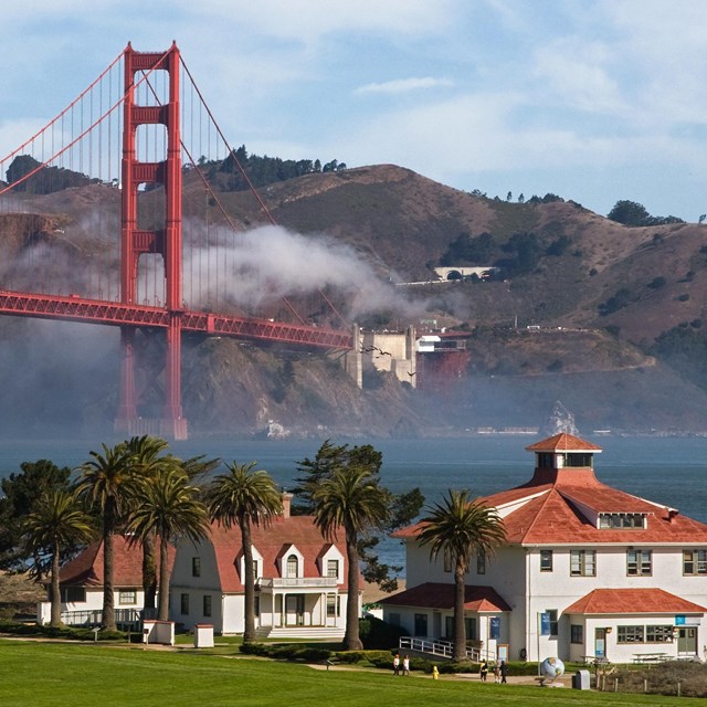white buildings with red roofs in foreground, golden gate bridge in background, blue sky beyond