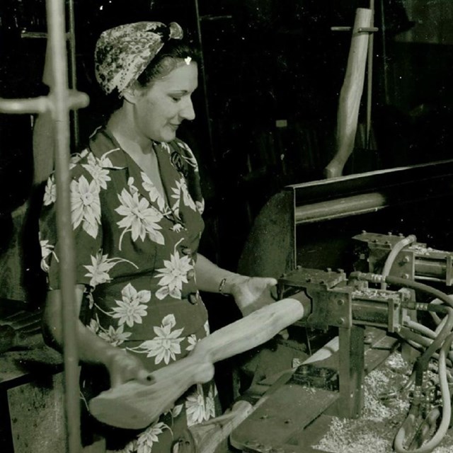 woman in floral dress and headscarf working at a munitions machine during WW2