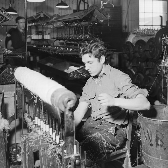 a man sitting and working at a silk weaving machine in a large factory 
